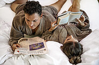 Pärchen liegt morgens im Bett und liest im Romantik-Wellnesshotel Winzer