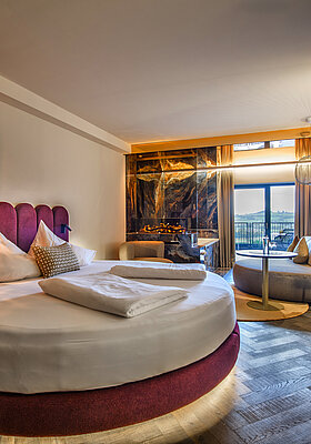 Sleeping area in the Kuscheltraum Deluxe Junior Suite at Hotel Winzer with a round double bed, fireplace, seating area and balcony