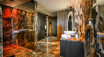 Offenes Badezimmer der Juniorsuite Kuschelnest Luxuriöses offenes Badezimmer der Juniorsuite Kuschelnest im Hotel Winzer mit Naturstein, Regendusche und beleuchtetem Spiegel